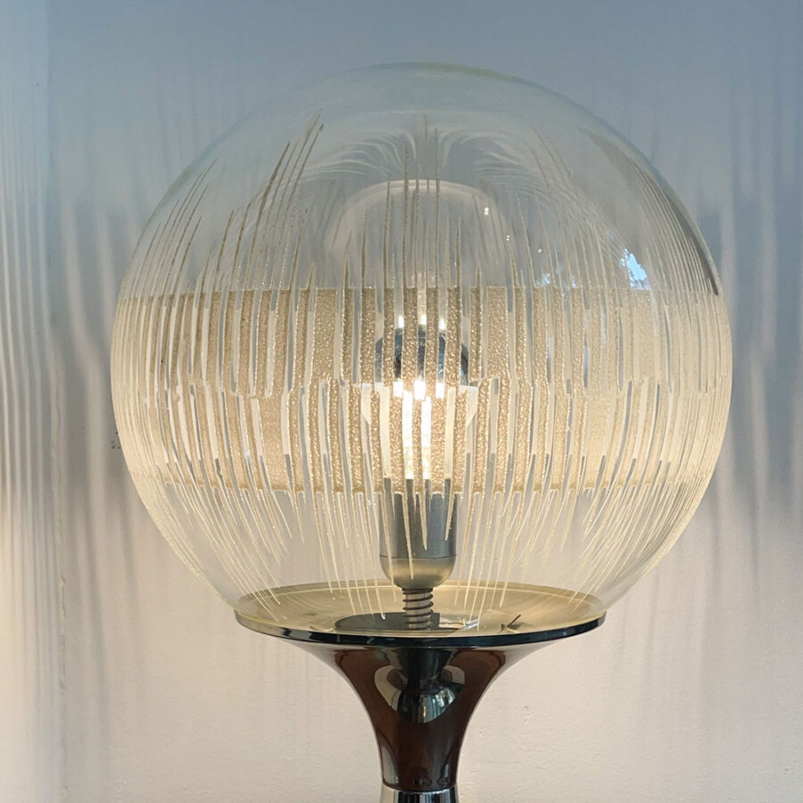 Die Tischlampe verkörpert durch und durch die Space Age Ära. Sie stammt aus den späten 1960er Jahren. Eventuell stammt sie aber auch aus dem Anfang der 1970er Jahre. Der Hersteller ist nicht mehr zurückzuverfolgen, da der Aufkleber, der auf eine Herkunft schließen würde, entfernt wurde. Die Authentizität der Tischlampe ist jedoch unverkennbar. Der Fuss verläuft aus einer tellerförmigen, flachen und runden Form zu einer Röhre nach oben, die sich zur Glaskugel hin wieder öffnet. Dort aufgestülpt befindet sich die Glaskugel und ist durch einen Federmechanismus auf dem Fuss gesichert.