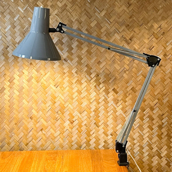 Die Vintage-Schreibtischlampe HCF DVE im freundlichen Industriegrau. Die Lampe stammt aus den 1970er Jahren und bezieht sich auf das klare Design Skandinaviens. Ihr schlankes Design zeigt eine außergewöhnliche Mischung aus Design und Funktionalität. Durch die Federn und die Feststellschraube am Gelenk lässt sich die Lampe verstellen mit einer maximalen Höhe von 88 cm. Die Lampe ist in einem schönen Vintage-Zustand und hat eine schöne Patina. Den Zustand entnehmt bitte den Bildern. Mit ihrer schlanken Form und ihrer dezenten Farbe läßt sich die Lampe super mit anderen Einrichtungsgegenständen kombinieren und ist eine coole Ergänzung für jeden Arbeits- oder Wohnbereich. Die Einstellmöglichkeiten lassen sich anhand ihrer markanten Form erkennen und erfühlen. Der An- und Ausschalter befindet sich am oberen Rand des Lampenschirms.