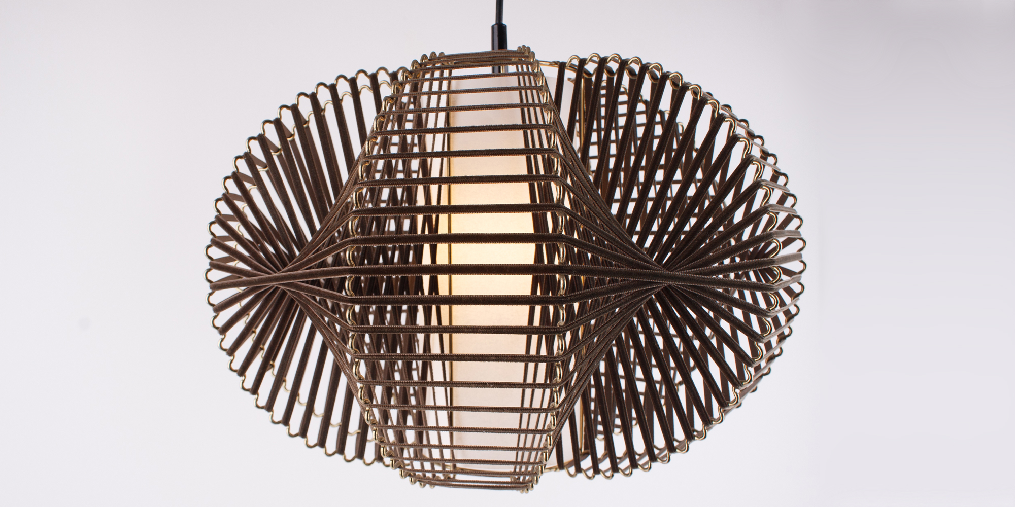 Eine Designlampe, bestehend aus Messing und Samtband. Die Art wie das Samtband auf den wellenartig geformten Draht gebunden ist, wirft ein tolles Licht auf die Zimmerwand. In der Mitte befindet sich ein Papier,das in Zilinderform das Leuchtmittel bedeckt und somit ein angenehmes Licht abgibt. Die Höhe der Lampe ist 30 cm und die breiteste Stelle an der Lampe ist 40 cm.